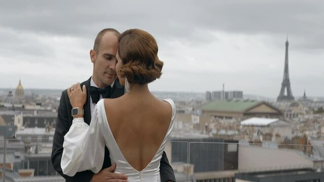 Couple enjoying each other on the background of Paris cityscape. Action. Elegant man in suit and woman in dress embracing in front of the Effel tower.