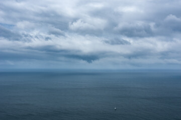 Ein einsames Segelschiff treibt mitten auf dem Ozean und über ihm dicke graue Regenwolken