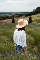 Portrait of a woman standing at the lavender field in a straw hat and white blouse