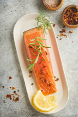 Salmon fish piece. Fresh raw salmon fish piece on marble board stand with herbs and lemon on light grey background. Seafood or menu concept. Top view.