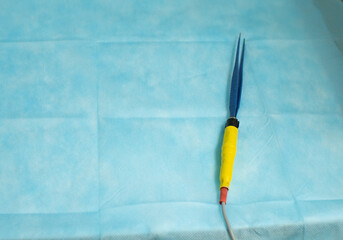 Electric bipolar tweezers to stop bleeding lie on the table against a blue background in the...