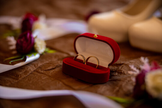 Two wedding rings in nice red box. Flowers and bride's white heels shoes around them on a bed. High quality photo
