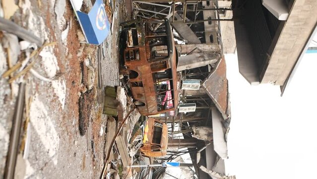 Metal frame of bus and car. Rusty body of bus and building near which transport turned into scrap metal from fire as result of shelling by rockets and bombs. War brings destruction and death