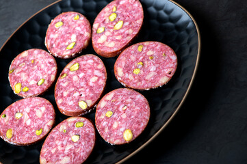 Traditional smoked salami sausage with spices and pistachios on black.Salami sausage slices on a...