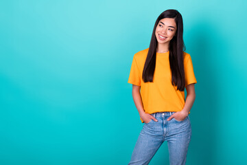 Photo of nice girlish pretty woman with long hair dressed yellow t-shirt look empty space hands pockets isolated on teal color background