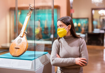 Interested young woman wearing protective face mask viewing collections of ancient musical...