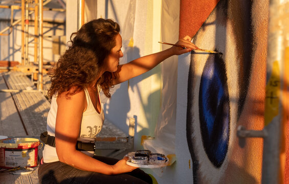 sexy female artist painter woman with curly brunette hair paints a street art peacock butterfly with brush and palette on the facade