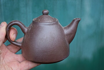 hand holding one old brown ceramic teapot on a green background