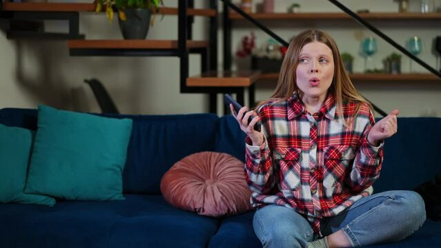 Stressed angry woman with smartphone sitting on couch on the right gesturing exhaling calming down. Portrait of displeased young Caucasian lady indoors at home in living room