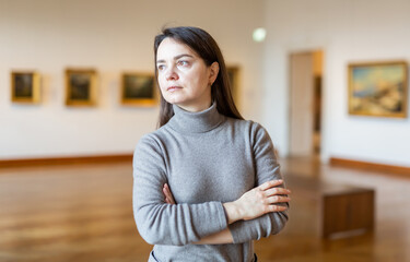 Obraz premium Positive brunette admiring artworks at paintings exposition walking in spacious museum hall..