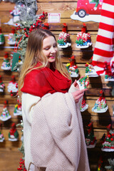 happy blond girl in red scarf close up portrait through Christmas decorated showcase on shopping mall background