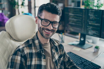 Portrait of cheerful hacker guy sit leather chair toothy smile operate pc server open space...