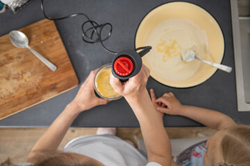 Woman and a child beat dough for baking with a mixer. Top view, flat lay