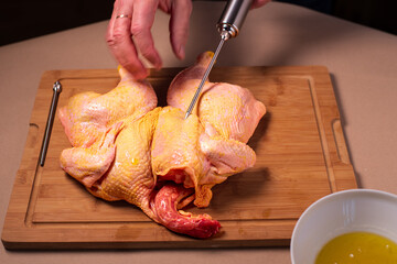 Chef prepares a whole raw chicken in the kitchen. Man prepares raw chicken for barbeque, injecting...