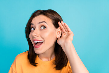 Portrait of positive astonished person arm near ear listen interested look empty space isolated on blue color background