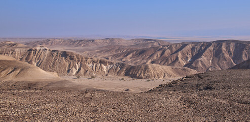 Colorful landscape of a remote region in Negev Desert near kibbutz Yahel seen from a hiking trail. Panoramic view of orange sandy hills, mountain folds and dry wide wadi Ya'alon. Vacation in Israel.