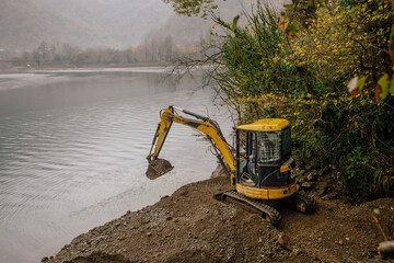 Light excavator at earthmoving works on the lake