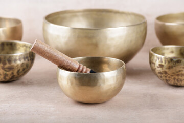Tibetan singing bowls with sticks used during mantra meditations on beige stone background, close up. Sound healing music instruments for meditation, relaxation, yoga, massage, mental health