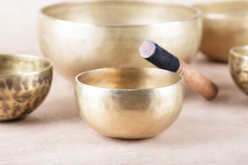 Tibetan singing bowls with sticks used during mantra meditations on beige stone background, close up. Sound healing music instruments for meditation, relaxation, yoga, massage, mental health