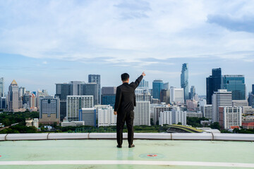 Full body shot of good-looking and confident businessman standing on tall building behind cityscape looking at goal