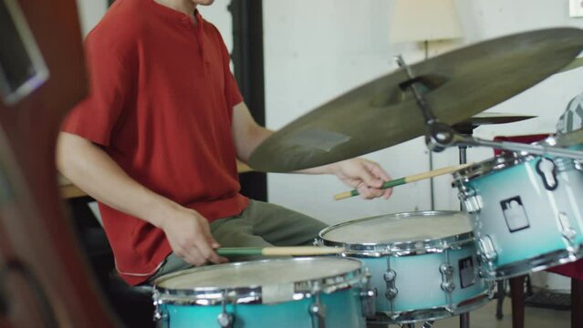 Young male musician playing drums while having rehearsal with band in studio