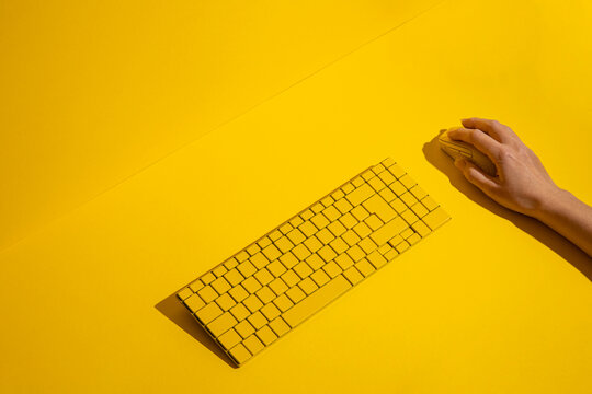 Female hand holds a yellow wireless mouse and keyboard on a blue background. Top view, flat lay