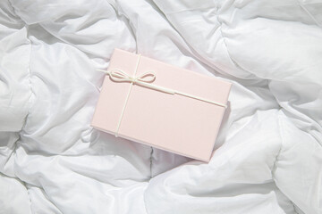 Light pink gift box on crumpled white fabric. Top view, flat lay