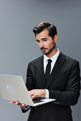 Man business looks into laptop and works thoughtfully online via internet in business suit video call business talks on gray background copy place