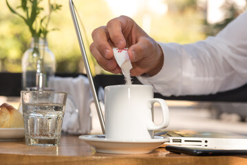 person putting sugar in their coffee, laptop on the table