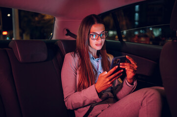 Business woman using smartphone while sitting in a backseat of a car at night