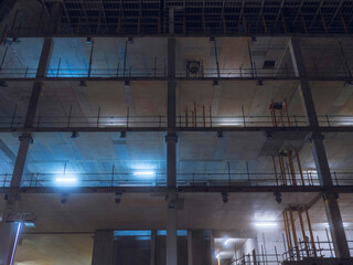 Construction site illuminated at night. Nobody. Strong concrete frame of a building. Building commercial and residential property.
