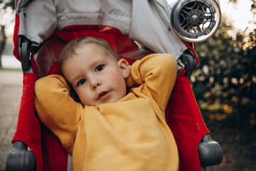 portrait of a 2-3-year-old child in close-up sitting in a red stroller on the sidewalk