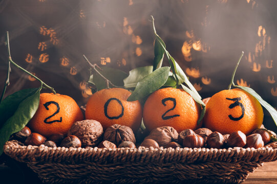 New Year 2023 is Coming Concept. Numbers written in Black Ink on clementines, oranges that are laying in the Basket with nuts in shells and Xmas Lights on the Background