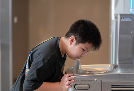 boy standing drinking water from a water dispenser