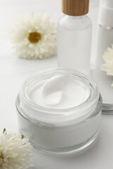 Fototapeta na wymiar Glass jar of face cream, different cosmetic products and flowers on white marble table