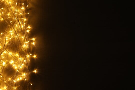 Beautiful glowing Christmas lights on wooden table, top view. Space for text