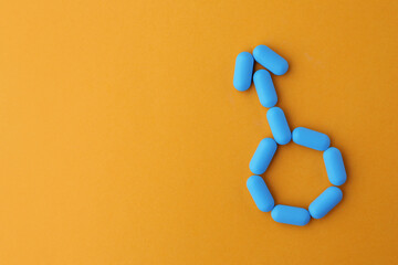 Pills and space for text on orange background, top view. Potency problem