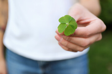 Woman holding beautiful green four leaf clover outdoors, closeup. Space for text