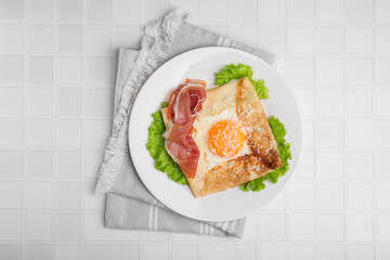 Delicious crepe with egg served on white tiled table, flat lay. Breton galette