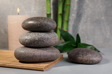 Fototapeta na wymiar Spa stones, bamboo and candle on light grey table, space for text