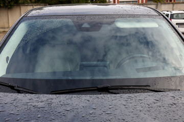 Car wipers cleaning water drops from windshield glass, closeup