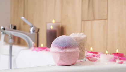 Obraz na płótnie Canvas Colorful bath bomb, sea salt, flower petals and burning candles on white tub in bathroom