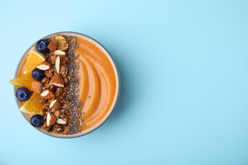 Bowl of delicious fruit smoothie with fresh orange slices, blueberries and granola on light blue background, top view. Space for text