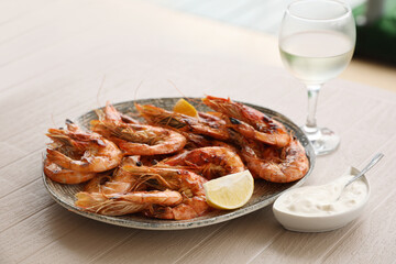 Plate of delicious cooked shrimps served with lemon, sauce and wine at table