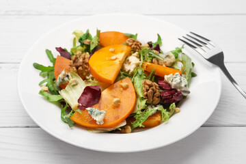 Delicious persimmon salad and fork on white wooden table, closeup