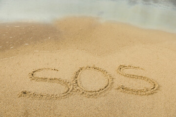 Fototapeta na wymiar Message SOS drawn on sand near sea