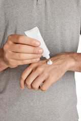 Man applying cream from tube onto hand on white background, closeup