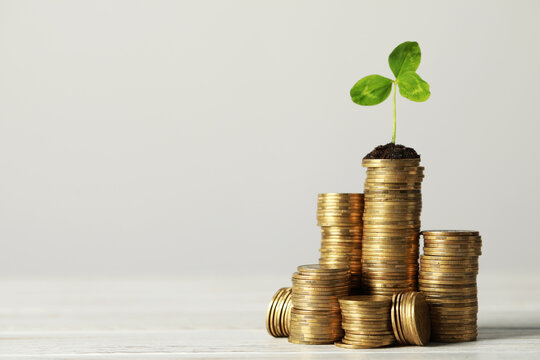 Stacked coins and green sprout on white wooden table, space for text. Investment concept