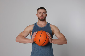 Athletic young man with basketball ball on light grey background