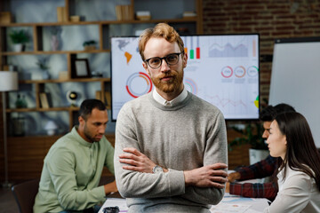 Confident smiling ginger guy, startup team leader, standing in front of mixed race office workers or business people with arms crossed or clasped, looking at the camera. business concept